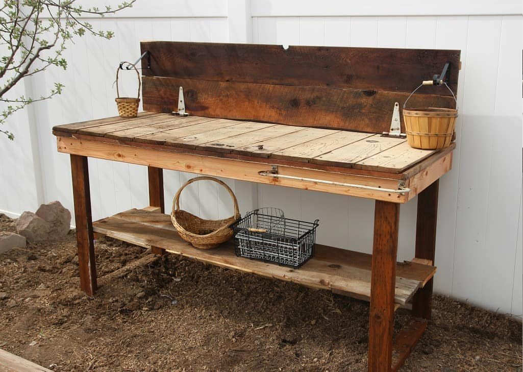 14 Reclaimed Wood Projects for Rustic Home Decor 4 Rustic wooden potting bench with baskets and wire bin against a white fence.