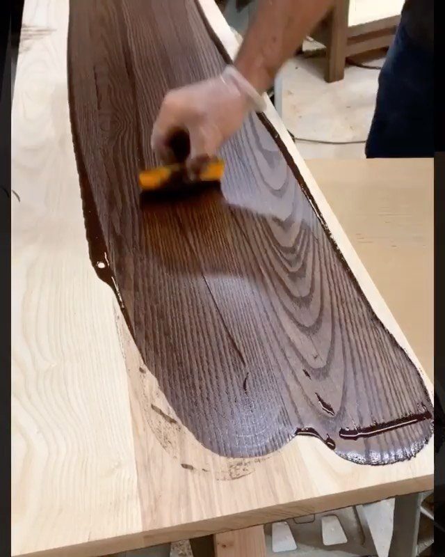 Hand applying a glossy protective finish to a dark wood board with a sponge.