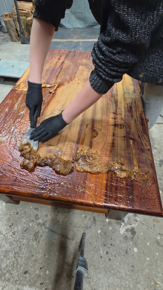 Person scraping chemical stripper off a wooden table during furniture refinishing process.