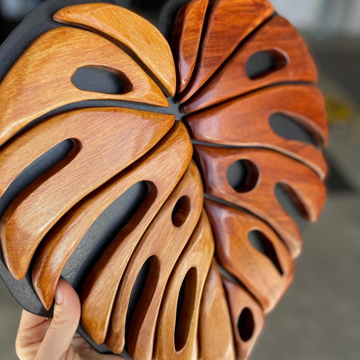Carved wooden monstera leaf sculpture with polished orange-brown finish on dark background