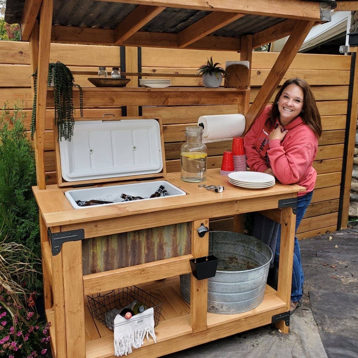 Rustic wooden outdoor beverage station with a built-in cooler and a woman smiling.