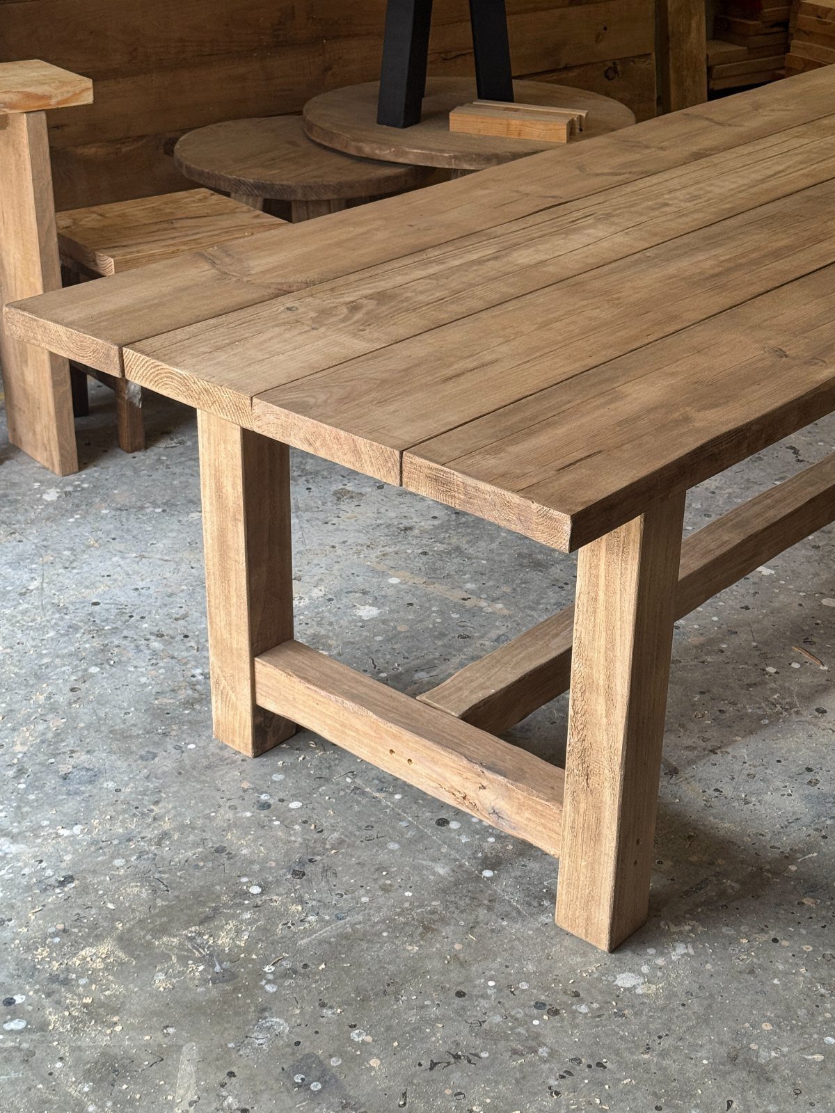 Rustic farmhouse dining table made from light brown reclaimed wood planks on concrete floor