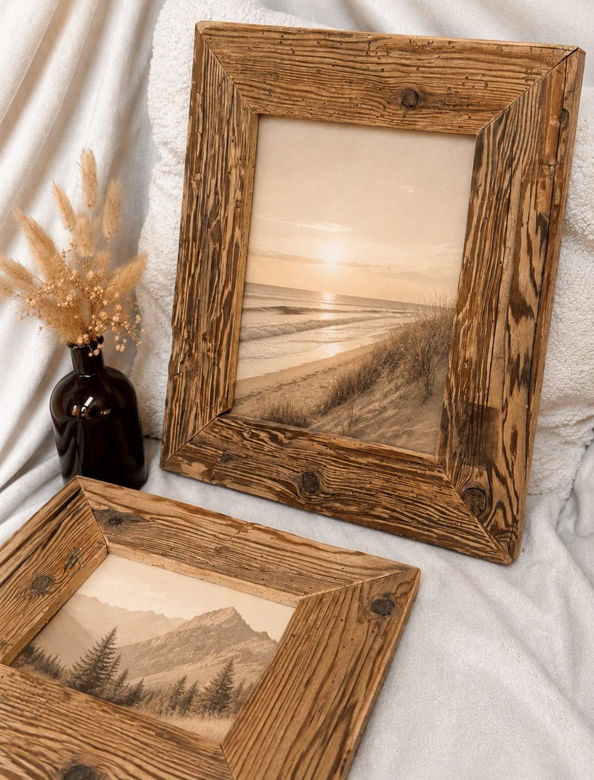 Rustic reclaimed wood picture frames with landscape art on a white fabric surface.