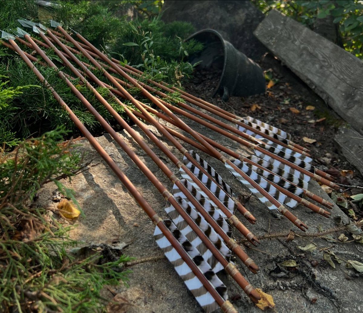 Handmade wooden arrows with striped feathers lying on a grey stone outdoors.