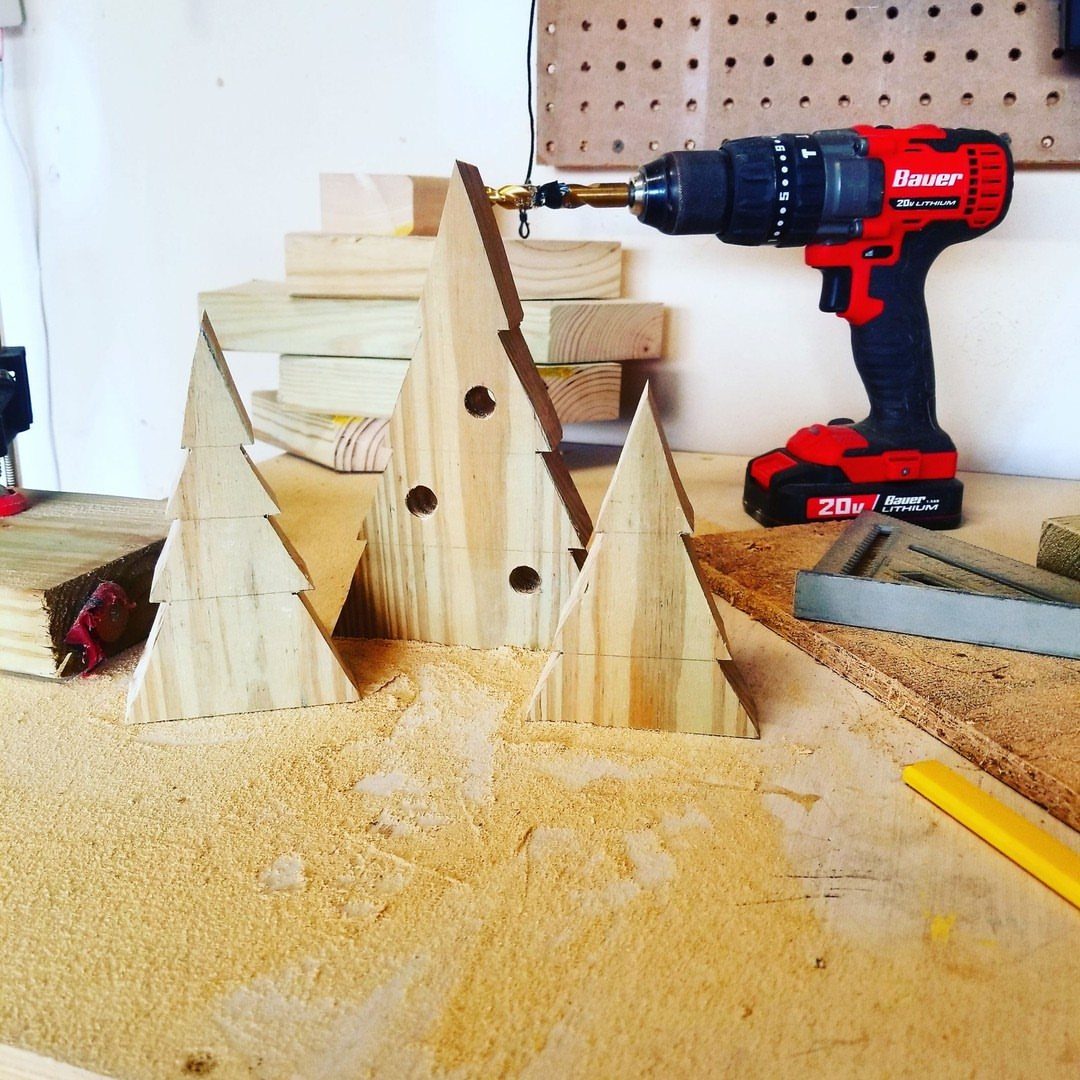 13 Scrap Wood Art Ideas for Using Up Your Leftover Boards 4 Wooden Christmas tree cutouts on a workbench with a red power drill.