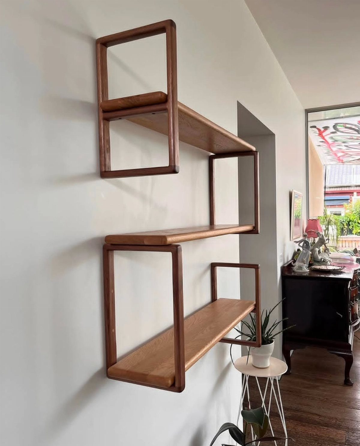 Geometric brown wood wall shelves with interlocking rectangular frames on a grey wall.