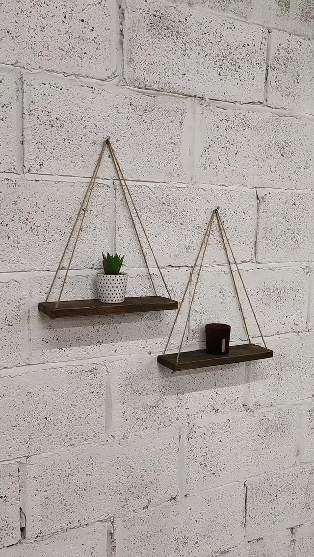 Two dark wood hanging shelves suspended by rope on a white brick wall.