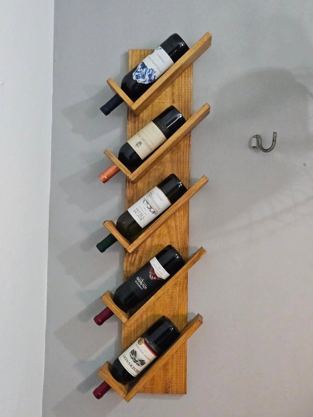 13 Small Wood Craft Ideas for Beginners and Scrap Wood 8 Wooden wall-mounted wine rack holding five bottles of wine in slanted slots.