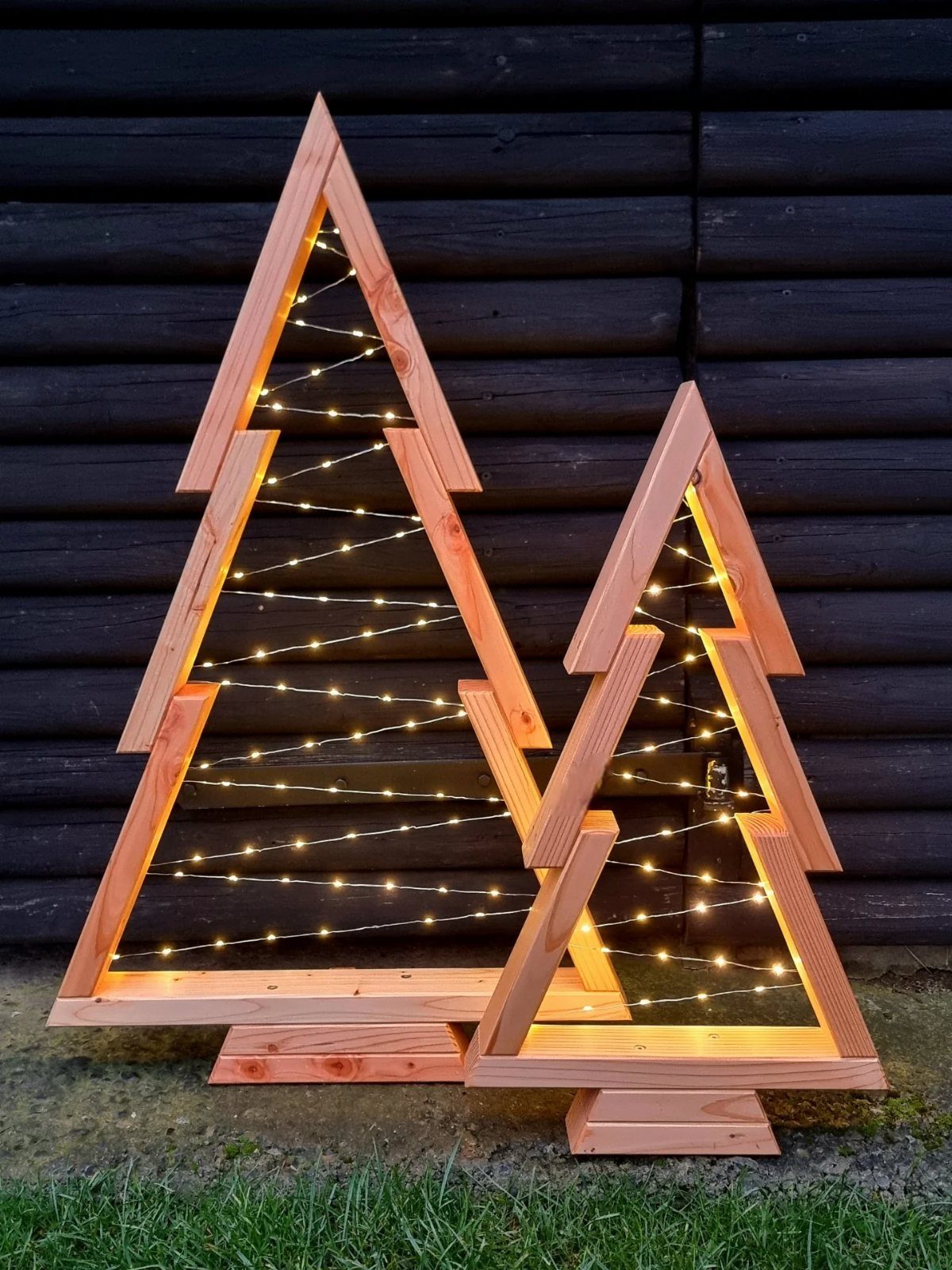 21 Small Wood Projects for Christmas You Can Make 3 Two wooden Christmas trees made of beams and decorated with warm fairy lights.