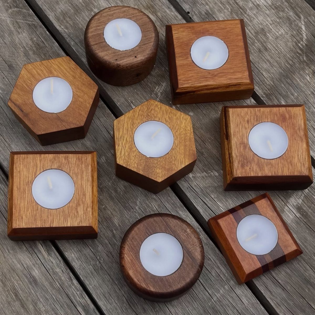 21 Small Wood Projects for Christmas You Can Make 4 Wooden candle holders in various geometric shapes holding white tea light candles on decking.