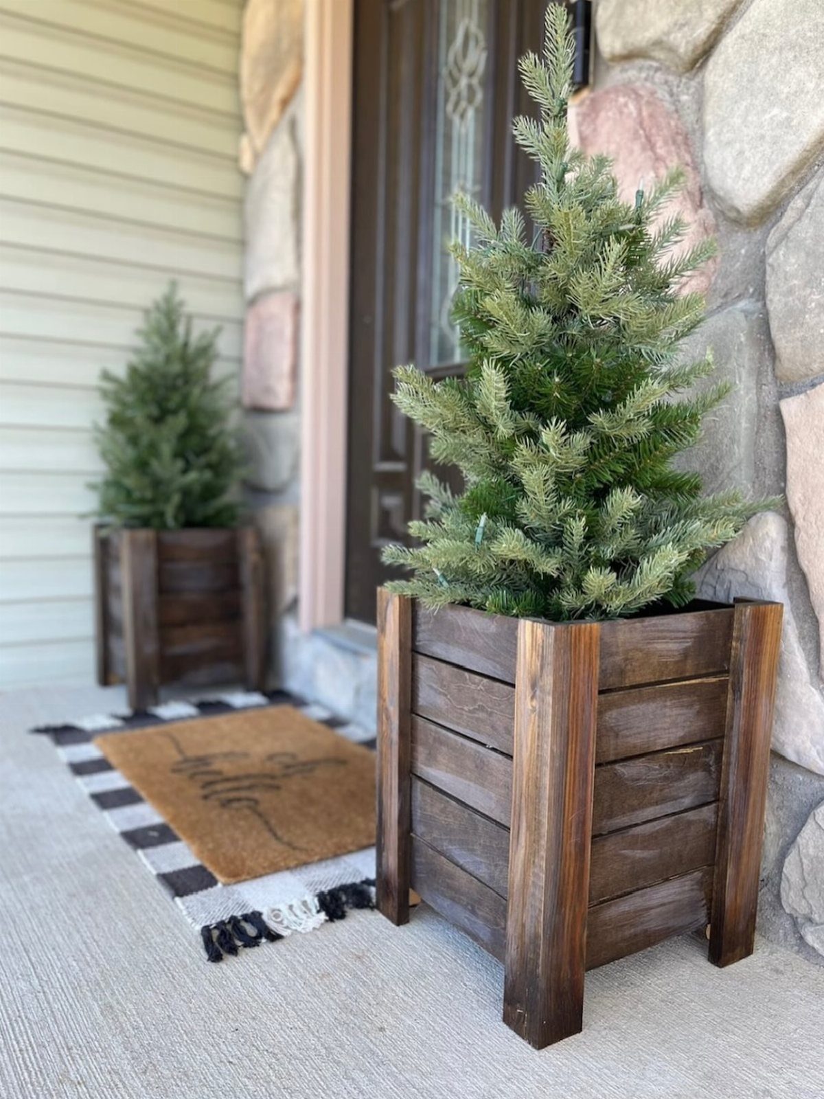 21 Small Wood Projects for Christmas You Can Make 8 Small evergreen trees in dark brown wooden slat planters on a home porch.