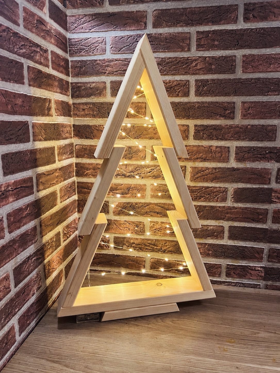 21 Small Wood Projects for Christmas You Can Make 6 Wooden Christmas tree shelf with warm fairy lights against a brick wall background.