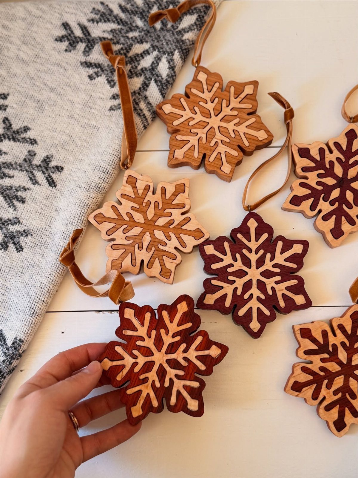 21 Small Wood Projects for Christmas You Can Make 5 Wooden snowflakes in different brown stains with leather loops on a white background.