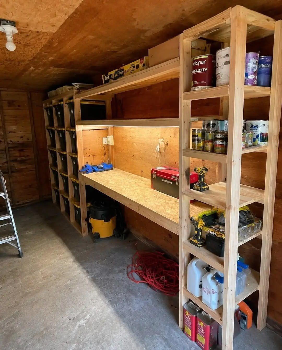 12 Small Workshop Storage Ideas for Tight Spaces 12 Wooden workbench with overhead shelving and a tall side shelf in a workshop.