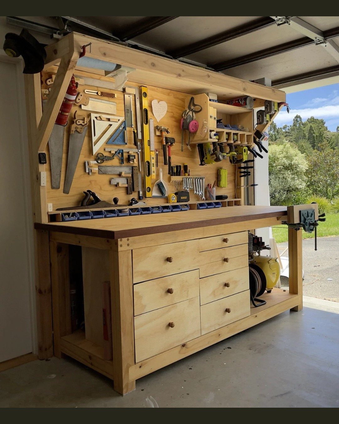 12 Small Workshop Storage Ideas for Tight Spaces 5 Wooden workbench with integrated under-bench storage cabinets and a tool-organized wall backdrop.