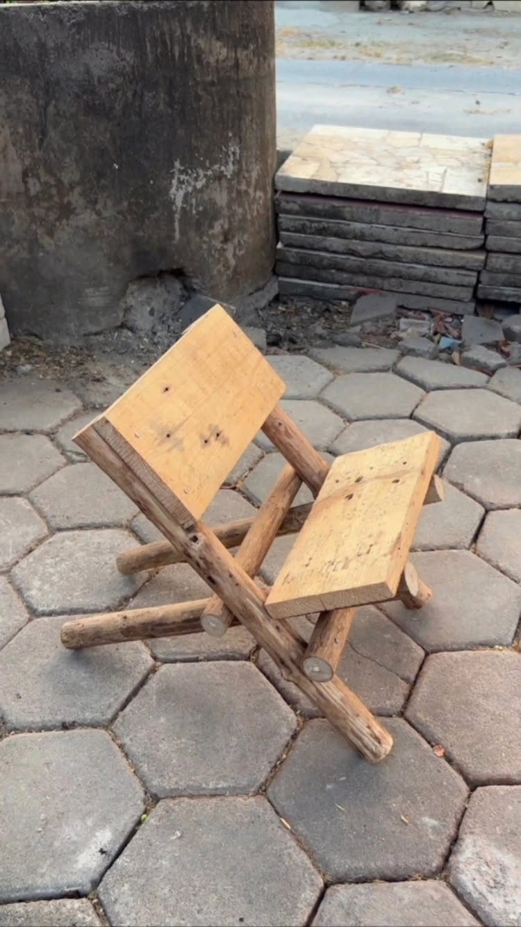 24 Summer Wood Projects for Beginners and Weekend Builders 22 Rustic folding chair made of light wood logs on grey hexagonal pavers.