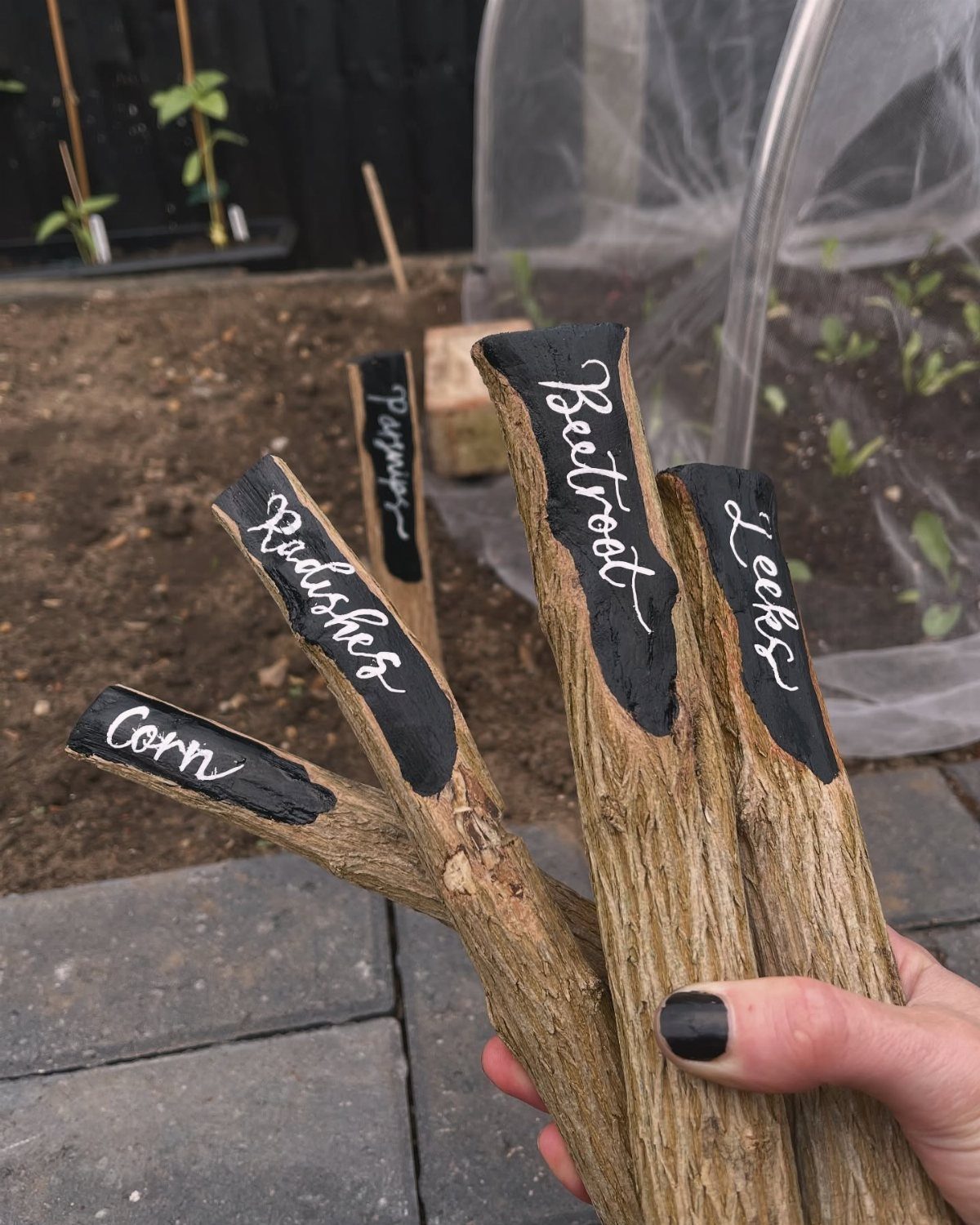 24 Summer Wood Projects for Beginners and Weekend Builders 18 Wooden garden markers made from branches with plant names written in white cursive.