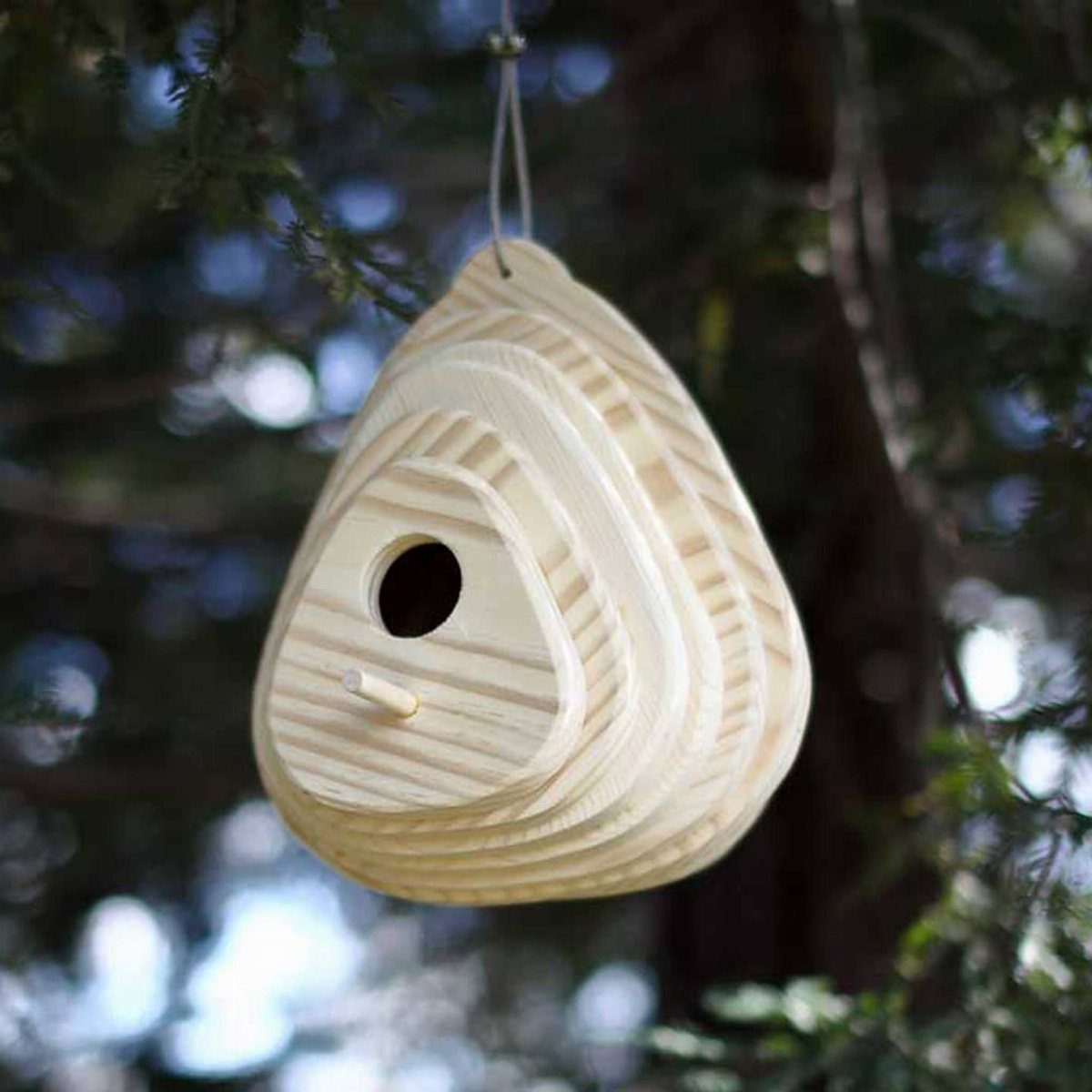 Layered wooden birdhouse hanging from a tree branch in a garden setting.