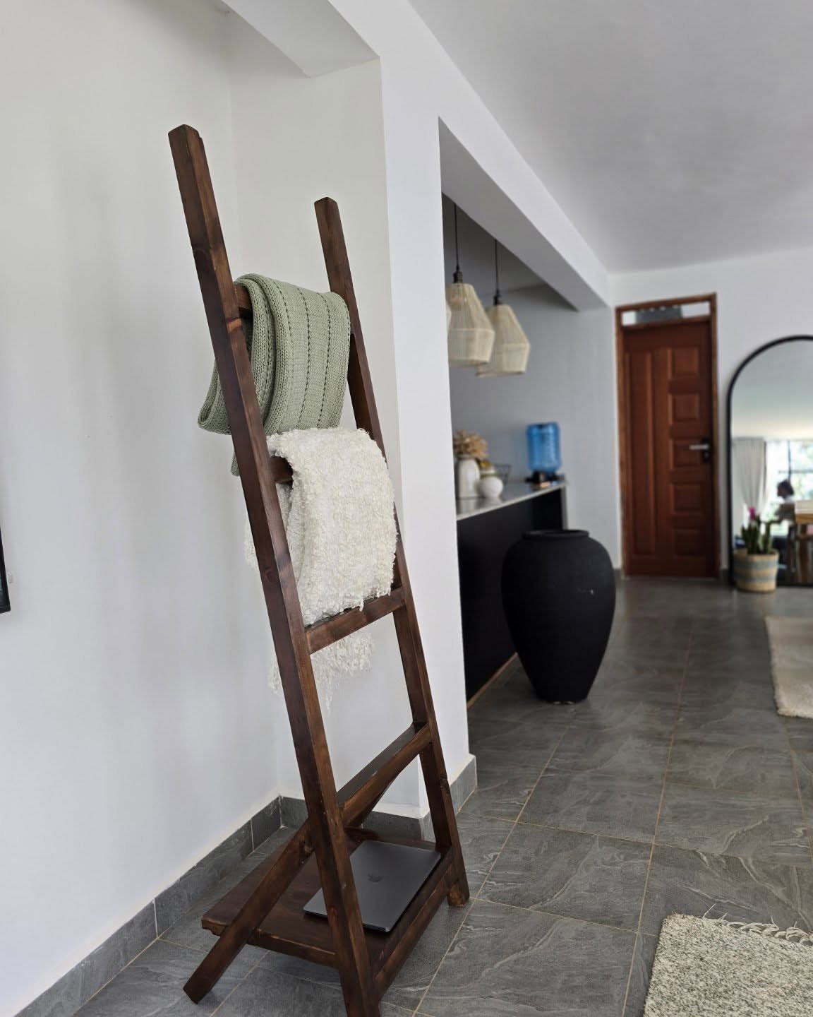 Wooden blanket ladder leaning against a white wall with two blankets draped over it.