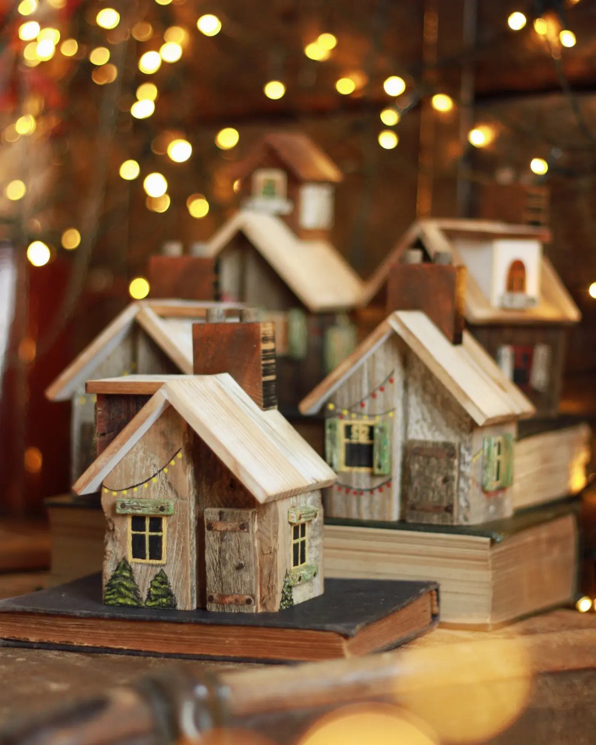 Small wooden model houses on old books with warm fairy lights in background.