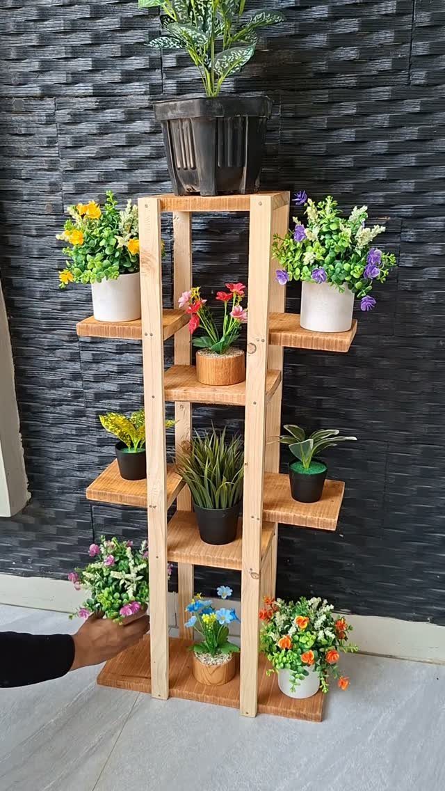 Multi-tiered light wood plant stand holding various colorful potted flowers and greenery.