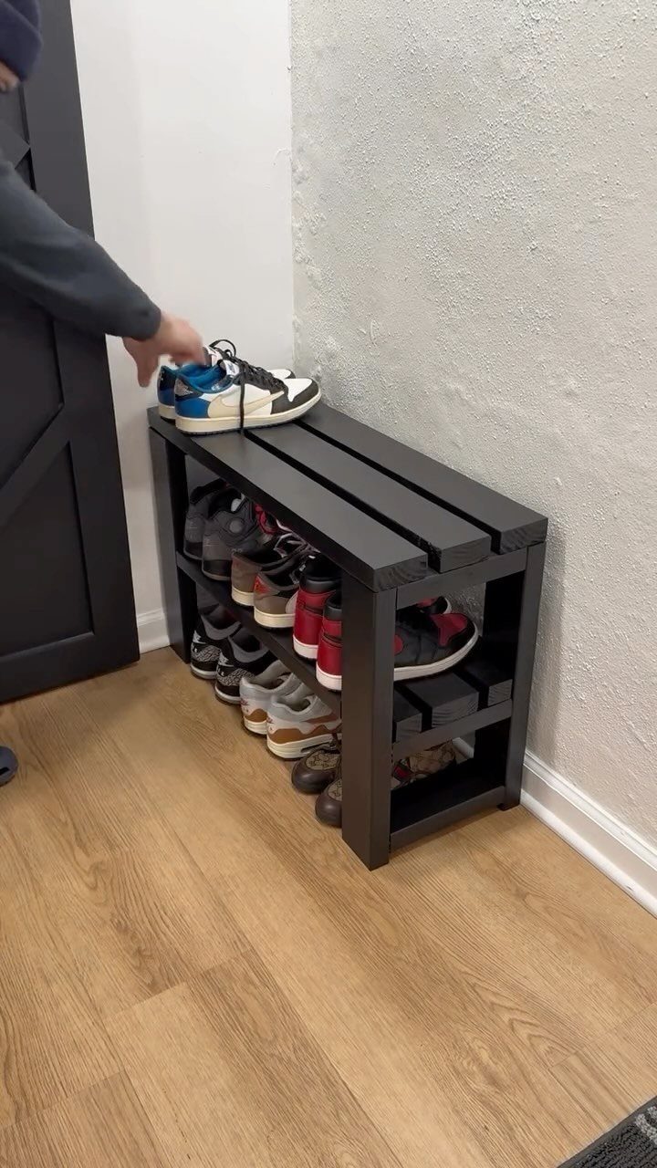 Dark grey wooden shoe bench with sneakers on a light wood floor.