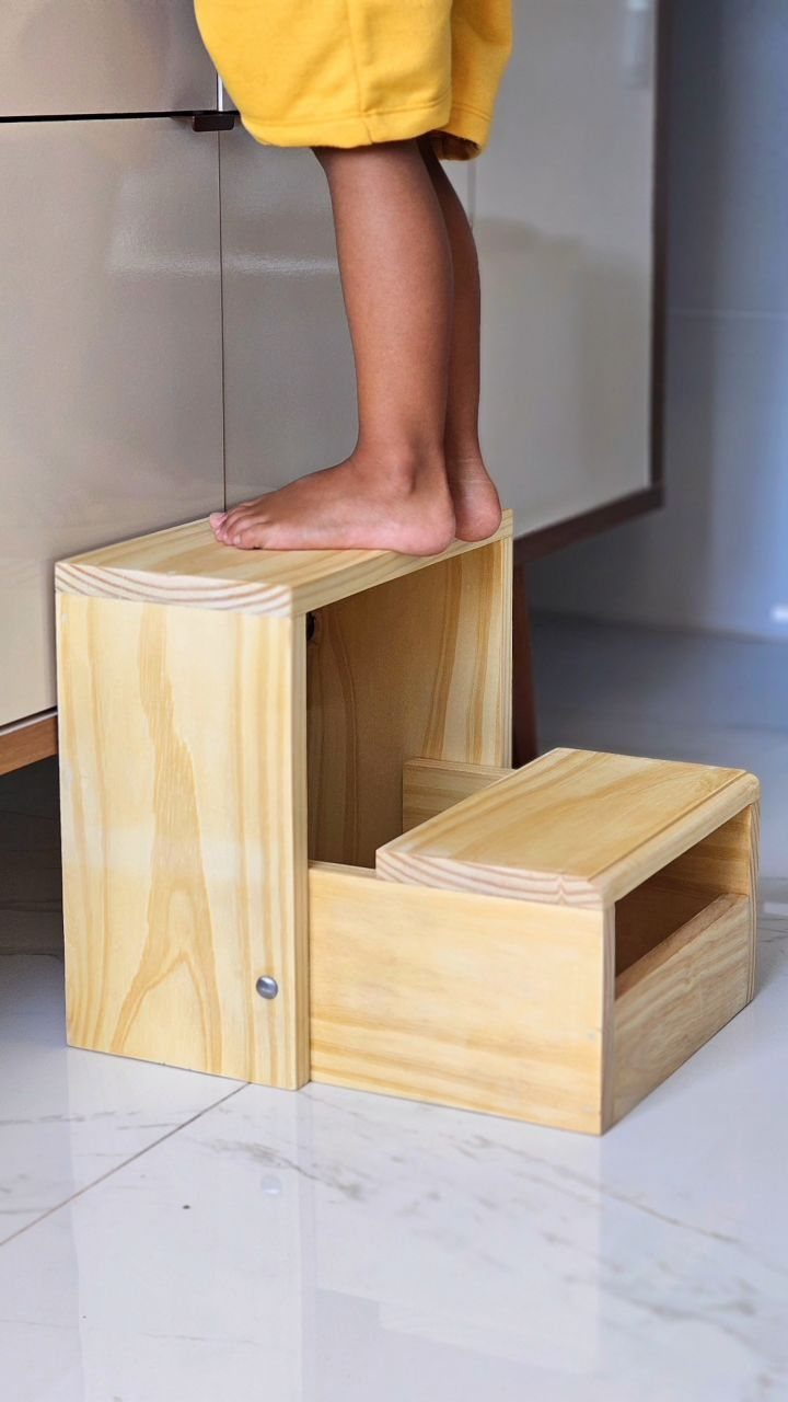 Wooden two-step stool with a child standing on the top step.