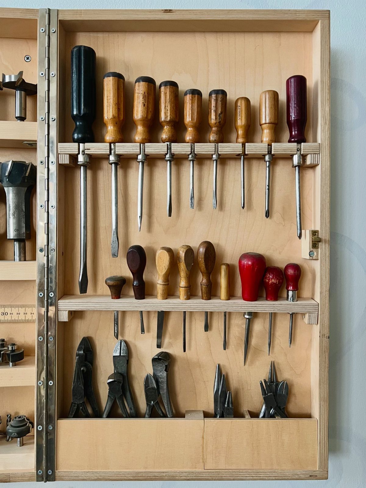 Wooden toolbox organizer with rows of chisels and pliers stored in a chest.