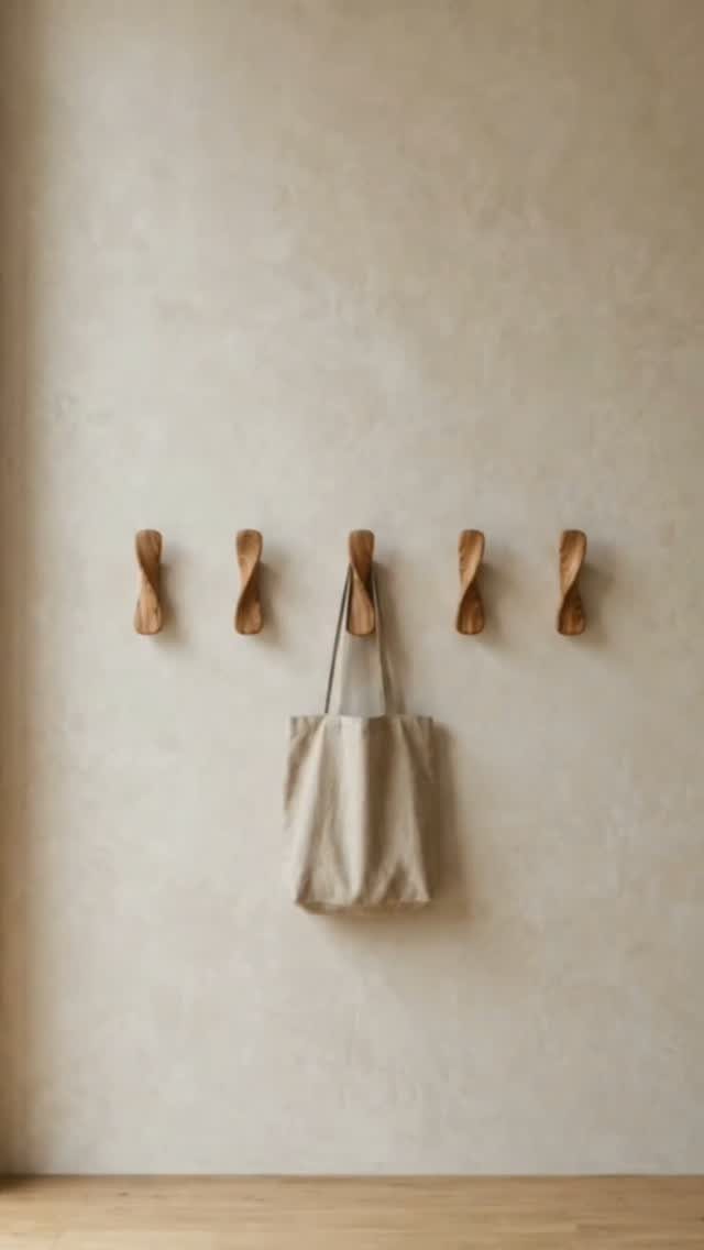 Twisted wooden wall hooks on a beige wall with a canvas tote bag.