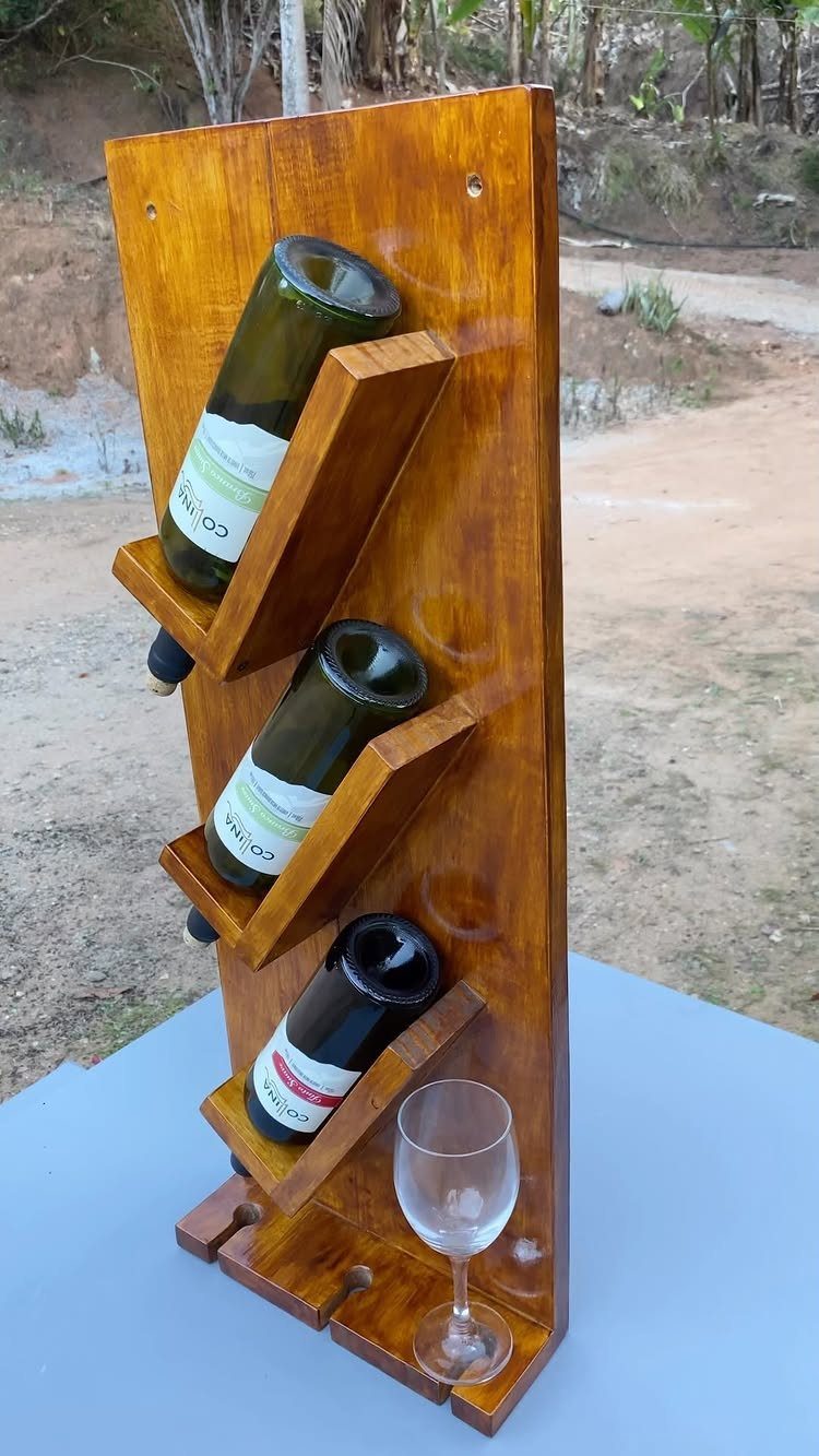 Wooden wine rack holding three bottles and a glass on a grey surface.