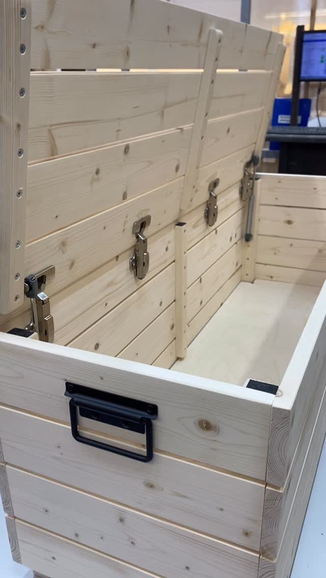 Wooden storage box with a hinged lid, metal latches, and a black side handle.