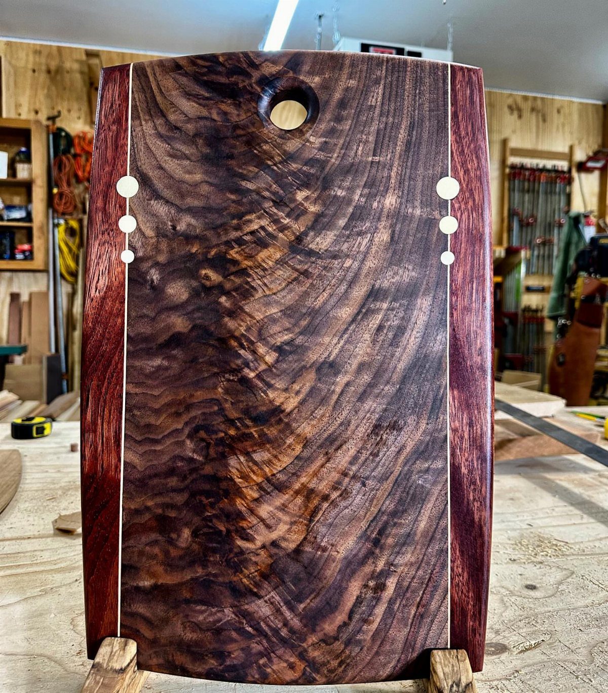 Polished dark wood cutting board with light inlay strips in a woodworking shop