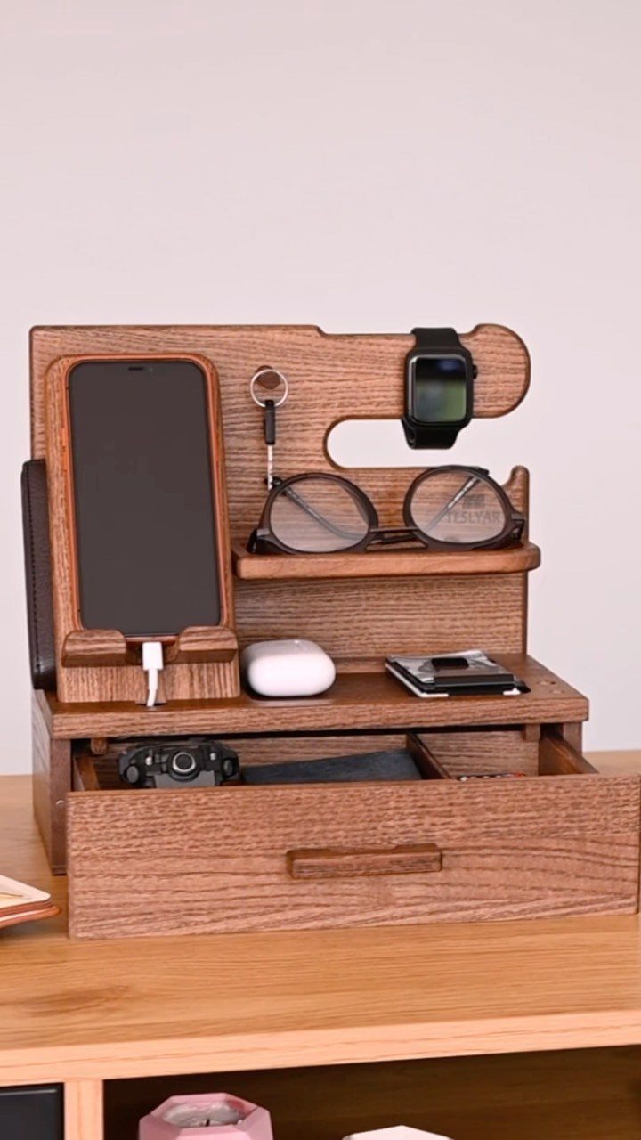 Wooden phone charging station holding a smartphone, smartwatch, glasses, and keys on a desk