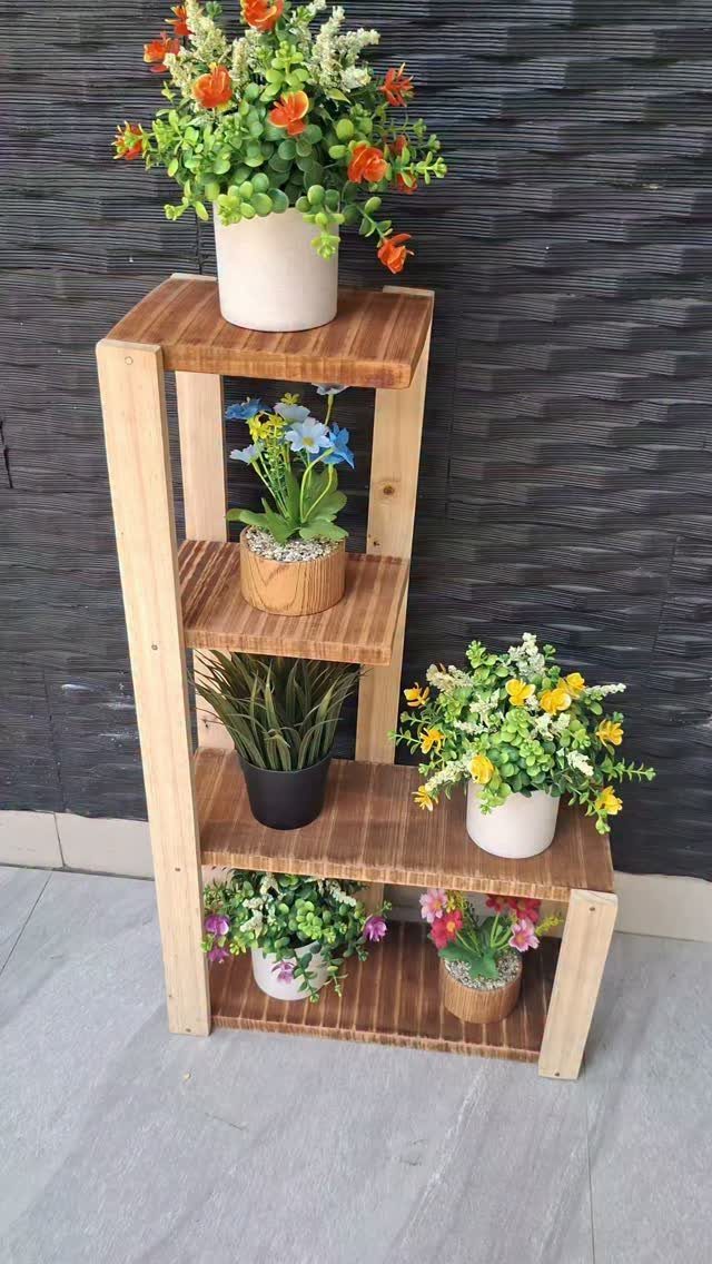 Wooden tiered plant stand holding several potted flowers against a dark textured wall.