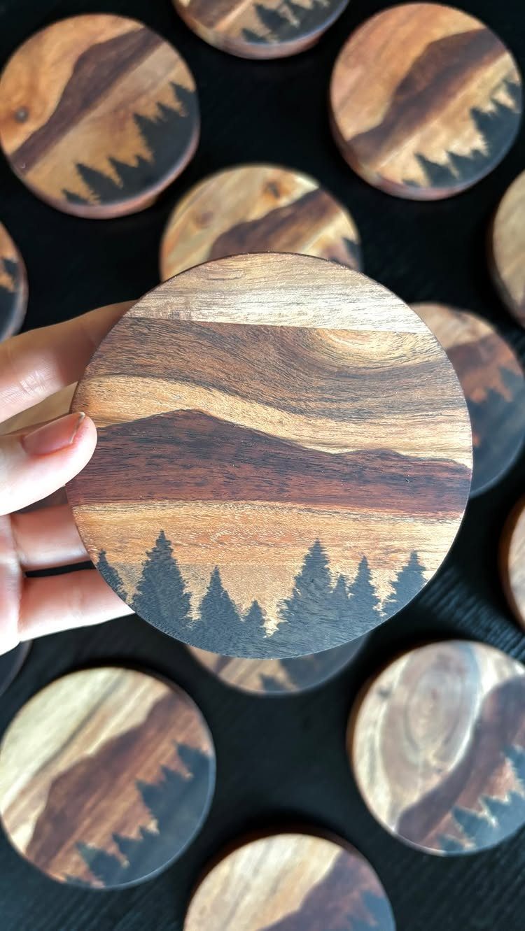 Circular wooden coasters with mountain and pine tree silhouettes on a dark background