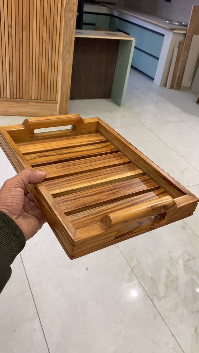 Wooden serving tray with slatted bottom and handles held by a person's hand.
