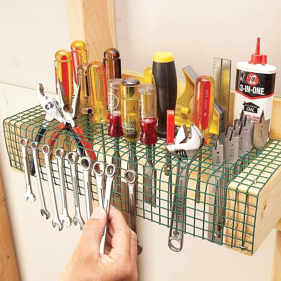Wooden tool organizer with green wire mesh holding various wrenches and screwdrivers.