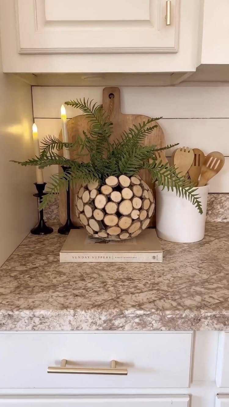 Round wooden log slice vase with a green fern on a kitchen counter.