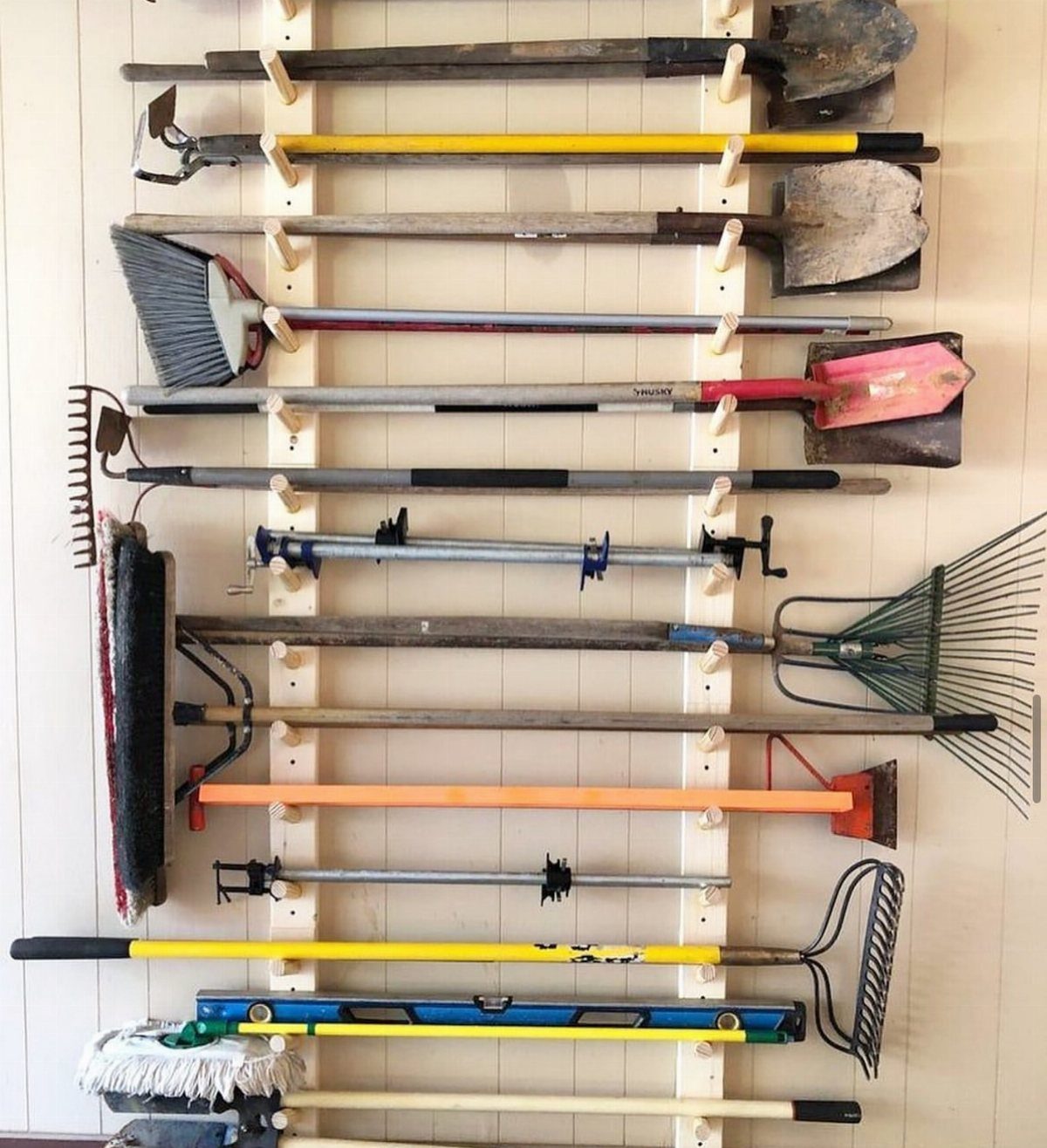 Tool Storage DIY Ideas: 7 Projects for Any Garage 6 Garden tools and brooms organized on a white wall with a wooden rack.