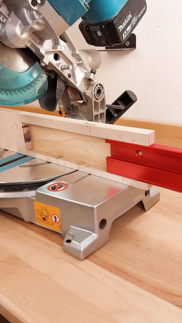 Miter saw cutting a light wooden board on a wooden workbench