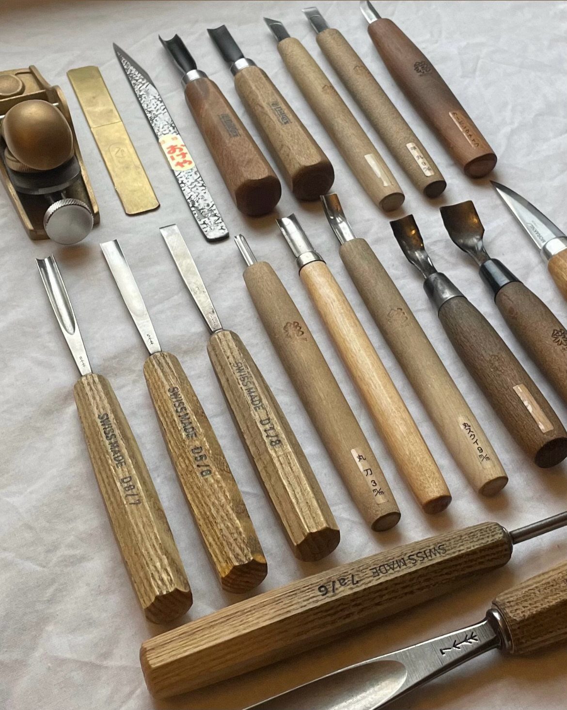 Various woodworking chisels, gouges, and a hand plane arranged on a white background.