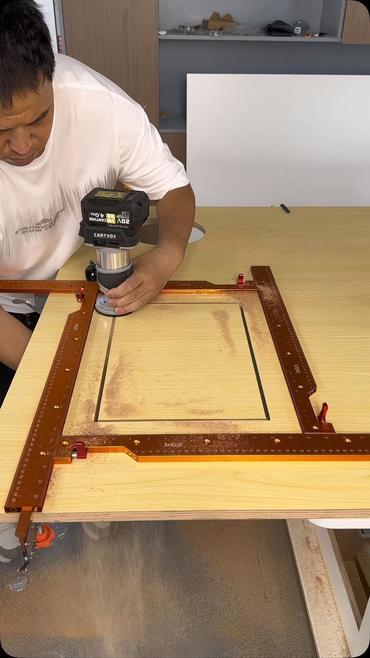 Man using a cordless router on a wooden board secured by a routing jig.