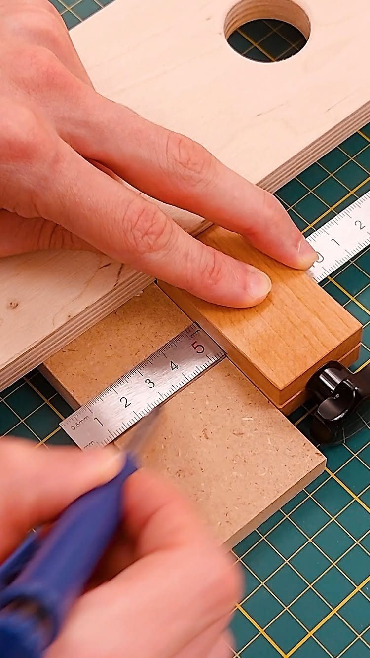 Hands using a marking knife and metal ruler on a piece of wood.