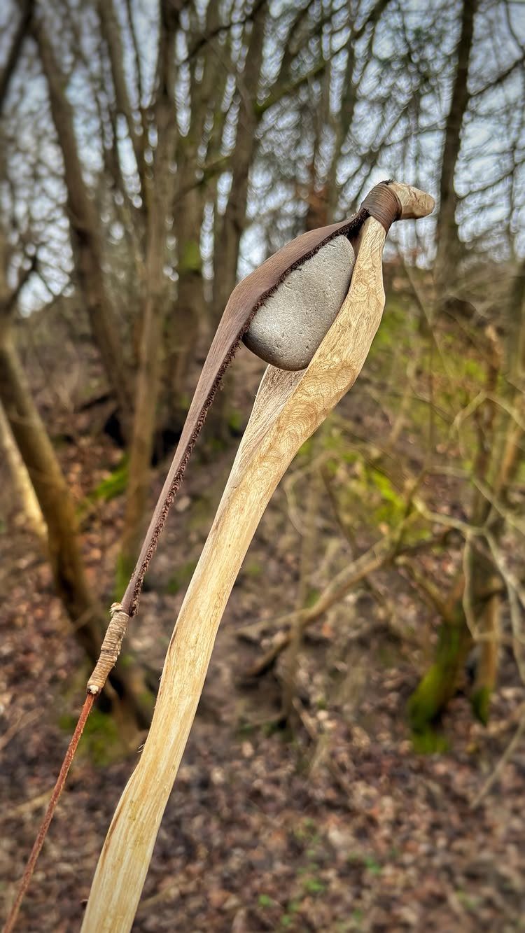 Carved wooden walking stick with a stone held by a leather strap in woods
