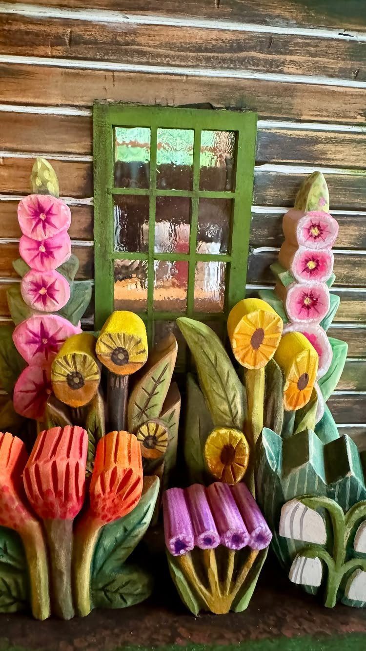 Colorful hand-carved wooden flowers arranged in front of a small green window frame.