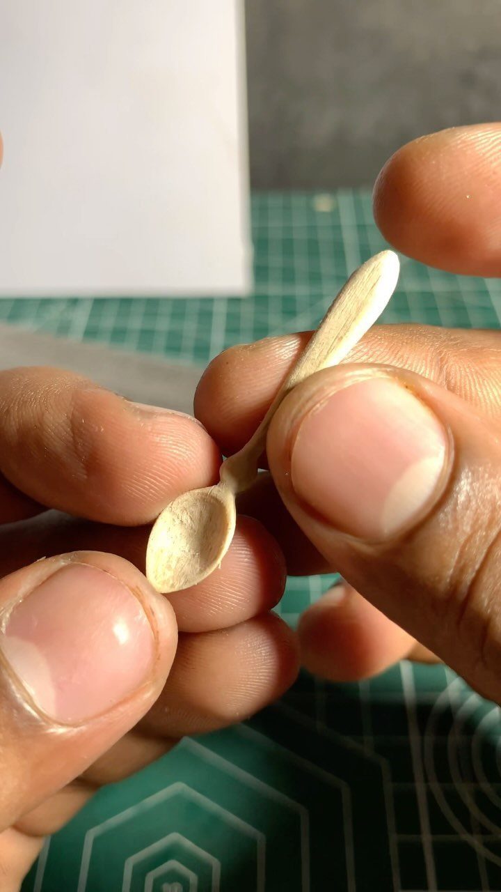 Small hand-carved wooden spoon held by a person over a green cutting mat