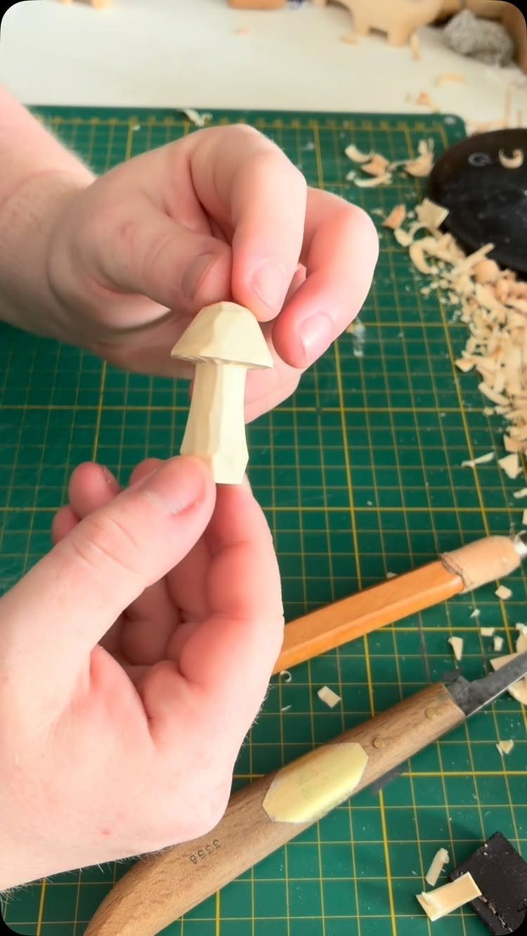 Hand-carved wooden mushroom held by hands over a green cutting mat with tools.