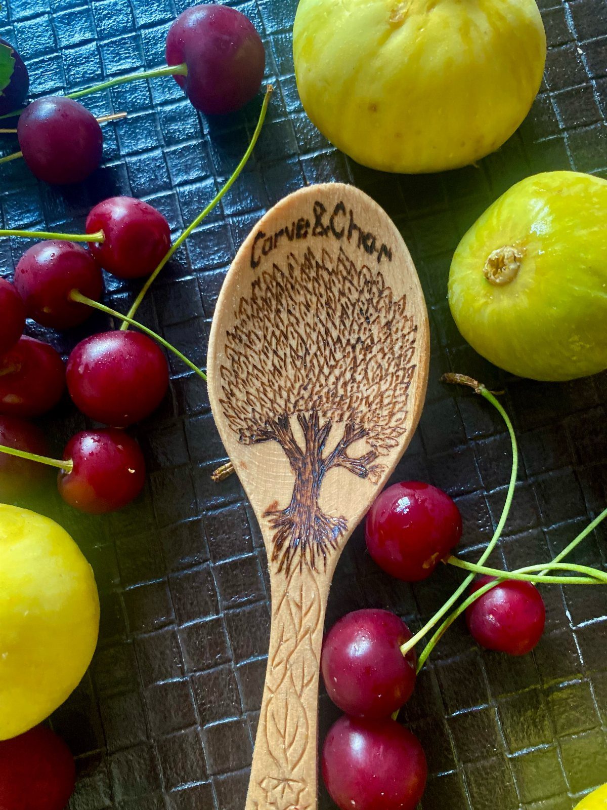 12 Wood Burn Designs for Beginners: Strokes and Patterns 10 Wooden spoon with a burned tree design surrounded by cherries and yellow fruit.