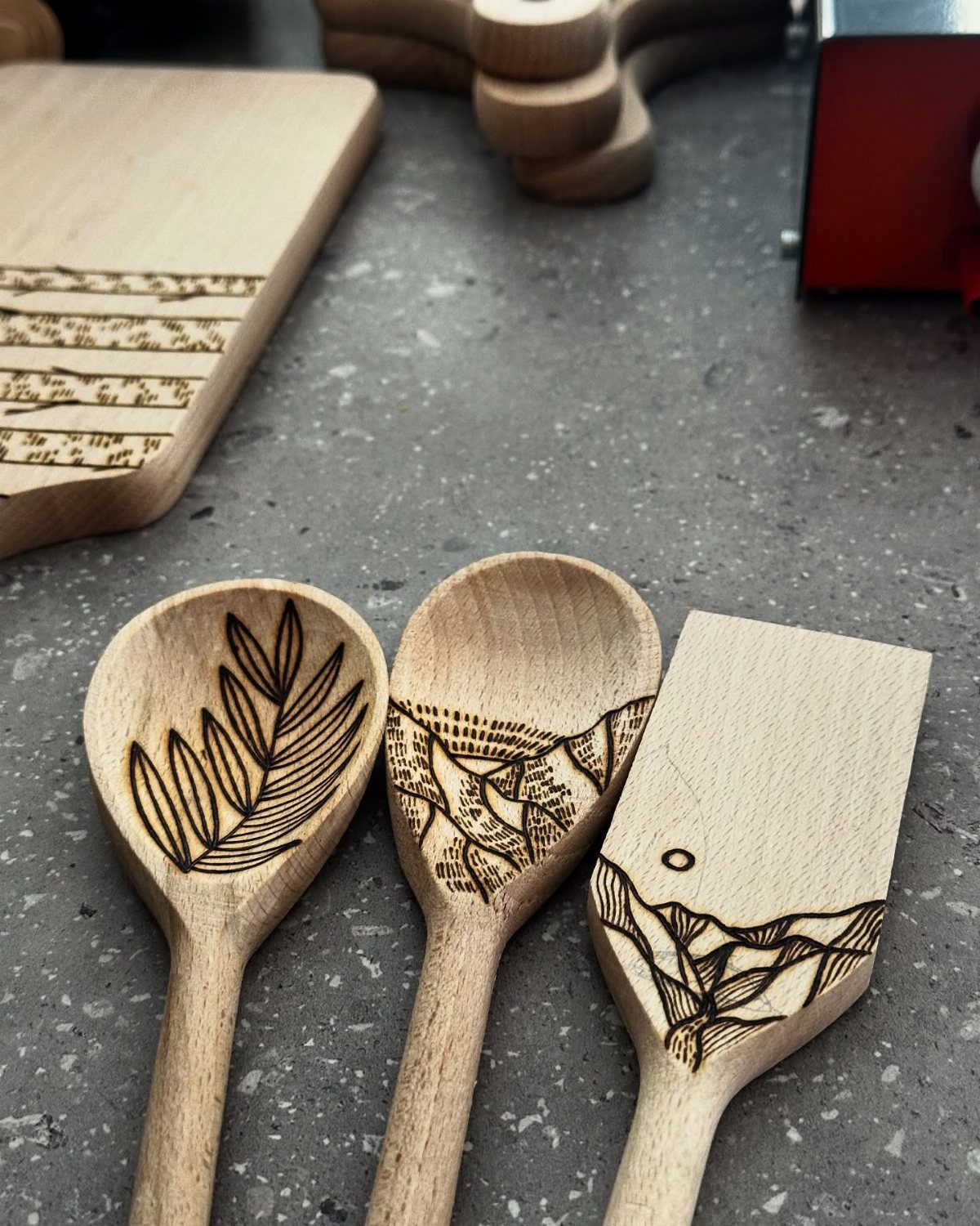 Wood Burning Art: 8 Ideas for Spoons, Coasters and More 3 Wooden kitchen spoons and a spatula with detailed wood-burned nature designs on a grey surface.