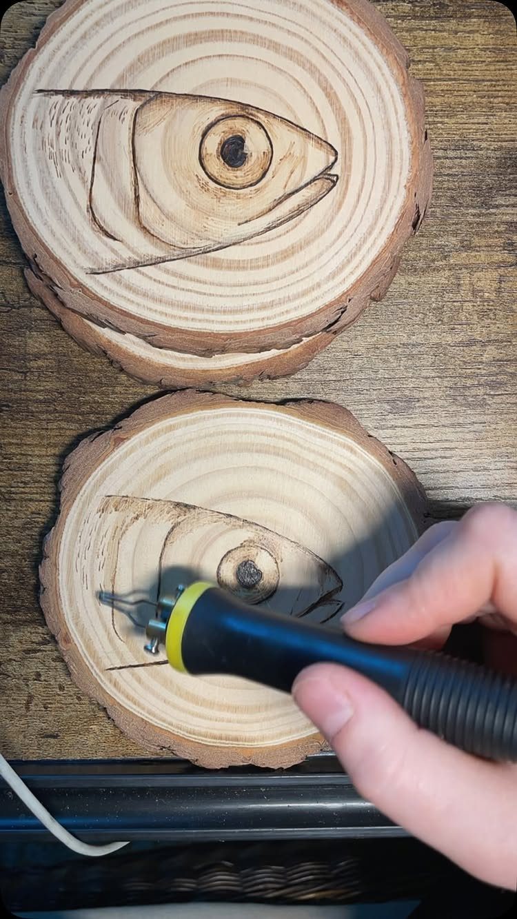 Wood burning tool etching a fish design into a circular wood slice coaster.
